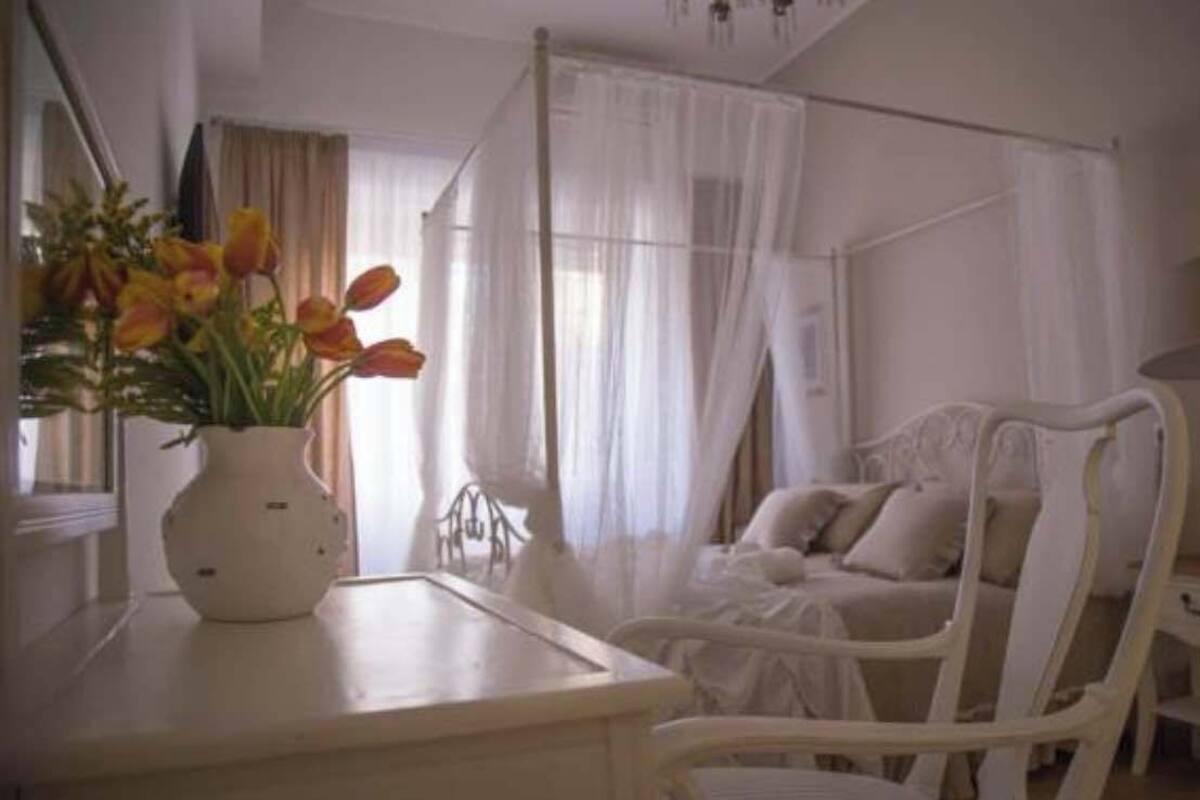 Ein Zimmer mit einem Bett, einem Sessel, einem Nachttisch und einer Vase mit Blumen.