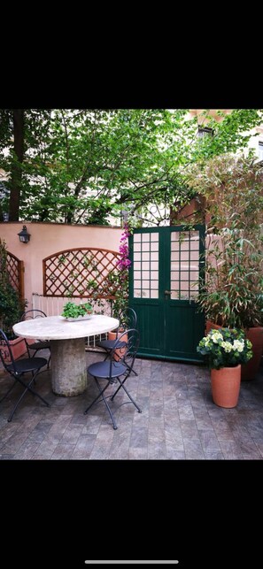 A patio with a round table and chairs, a green gate, and potted plants. - la piazzetta delle regine (Rome)
