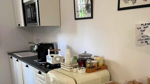 Eine kompakte Küche mit Kühlschrank, Mikrowelle und Kaffeemaschine. An der Wand hängen gerahmte Bilder und ein Schild, das anzeigt, dass die Küche geschlossen ist.