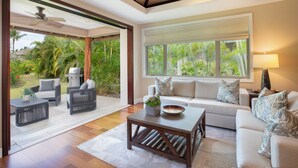 A spacious living room with a large sliding glass door leading to a patio area. Inside, there is a white sofa, a dark wooden coffee table, and a ceiling fan.