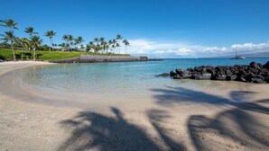 A beach with clear water, palm trees, and a rocky shoreline.