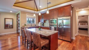 A spacious kitchen with wooden cabinets, a large island with bar stools, stainless steel appliances, and pendant lighting.