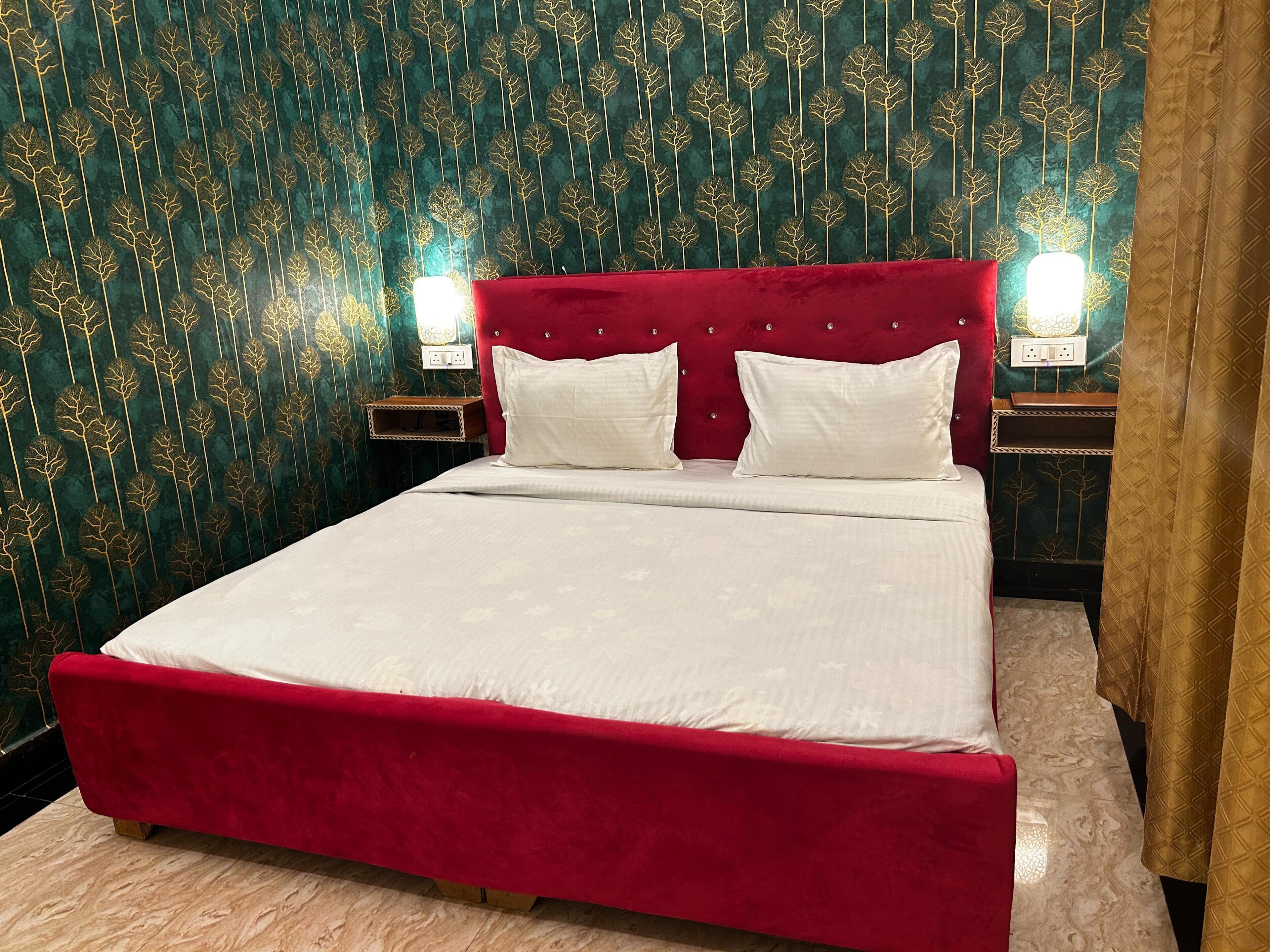 A bed with a red headboard and white bedding in a room with patterned wallpaper and a nightstand with a lamp.