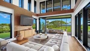 A modern living room with a large sectional sofa, a coffee table, and a TV mounted on the wall. - Luxury 6BR Hale o ka Nene Estate w/ Pool/Spa & Golf Views, Near Beach (Koloa)