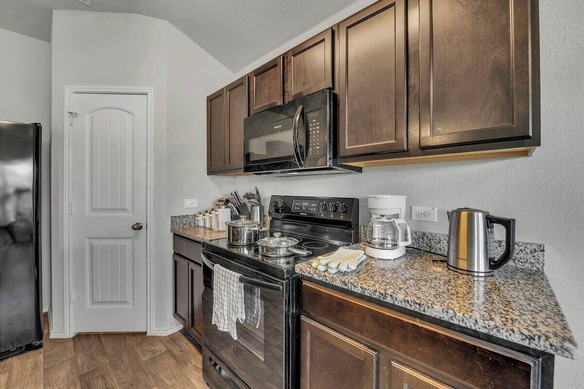 A kitchen with dark wooden cabinets, a stainless steel microwave, a stove, and granite countertops.