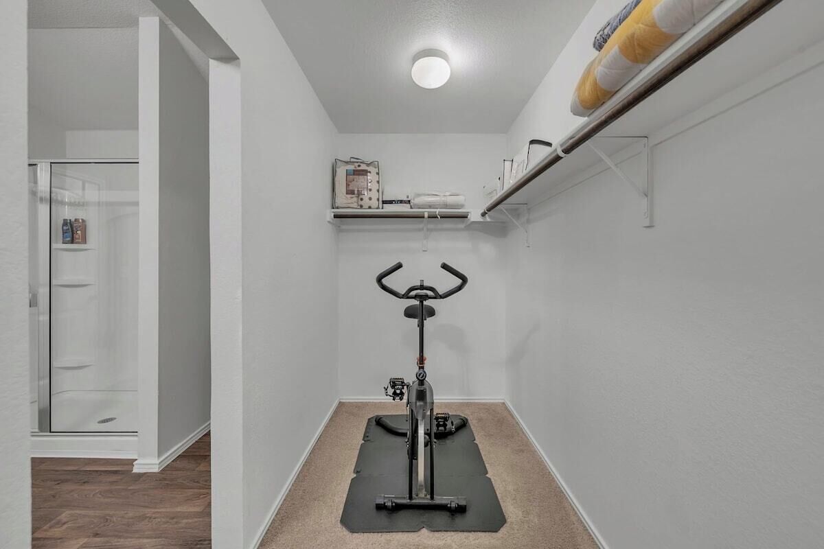 A compact room with a stationary bike on a mat, a glass shower enclosure, and a white door.