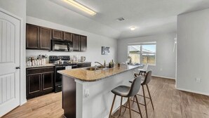 Une cuisine moderne avec des meubles de couleur bois foncé, un plan de travail en granit et un îlot central doté de tabourets de bar.