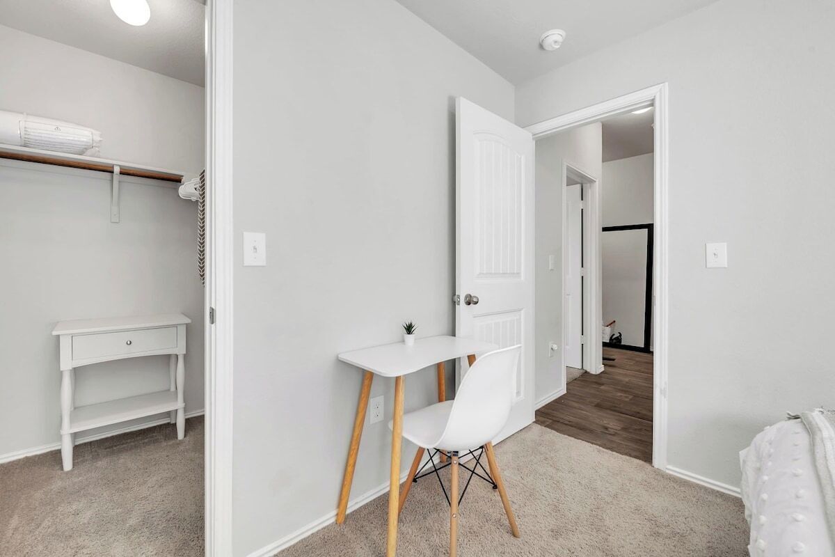 A room with a white desk, chair, and a small shelf.