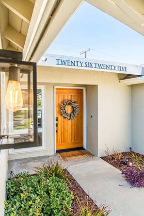 A modern house with a wooden front door, a welcome mat, and a wreath. - @ Marbella Lane - Cozy Modern Home w/ Relaxing Design & Pool (Fullerton)