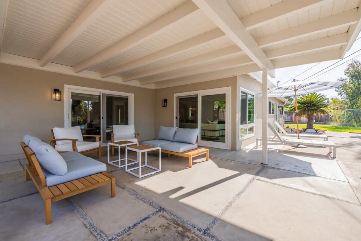 A covered outdoor seating area with wooden furniture and a concrete floor.