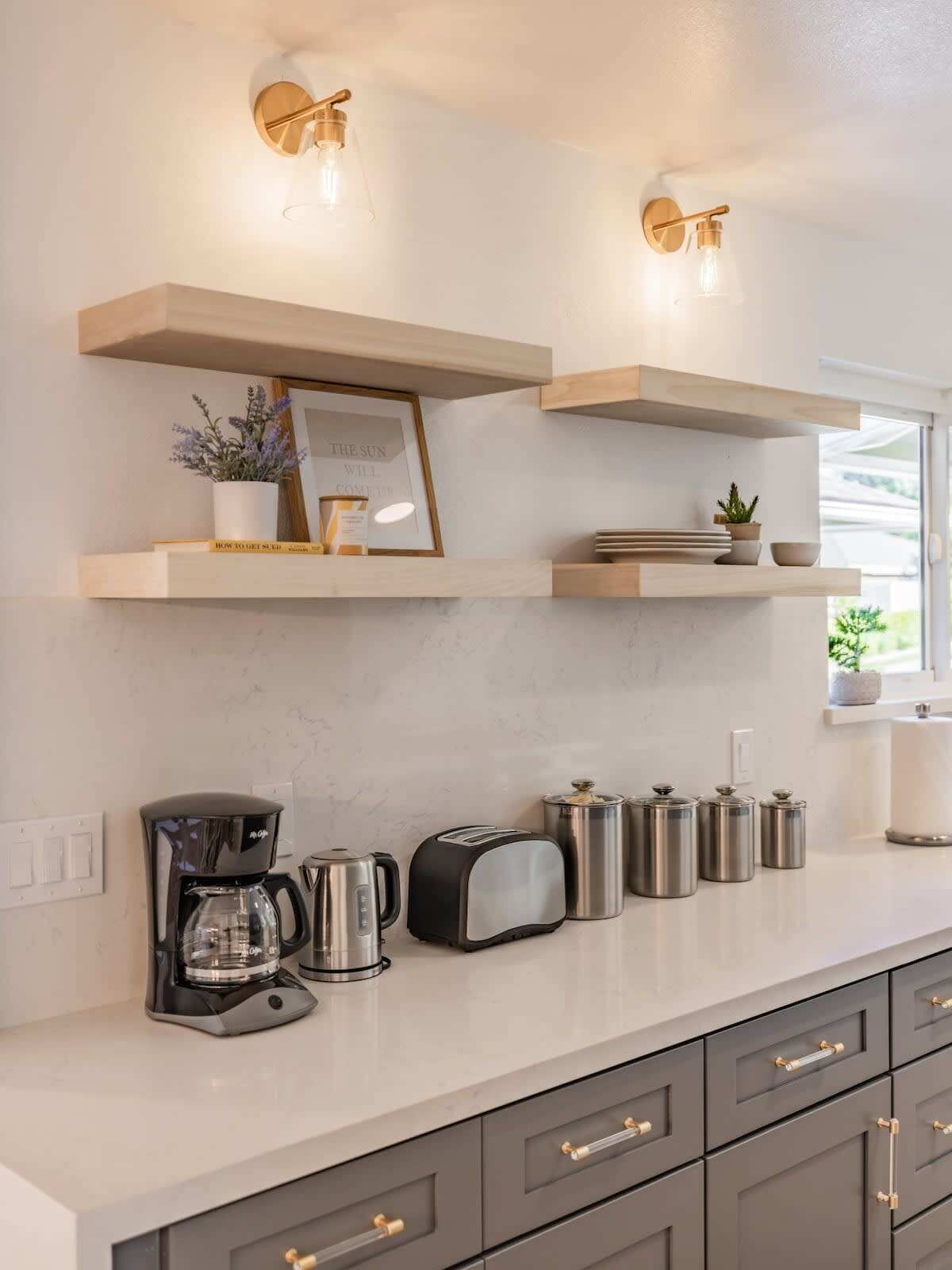 A kitchen with wooden shelves, a coffee maker, a toaster, and stainless steel containers.