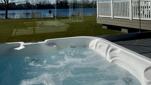 Ein Whirlpool mit freiem Blick auf einen See und eine Holzterrasse mit Geländern.