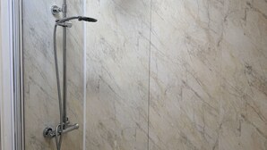 A modern bathroom with a glass-enclosed shower, a freestanding bathtub, and marble walls.