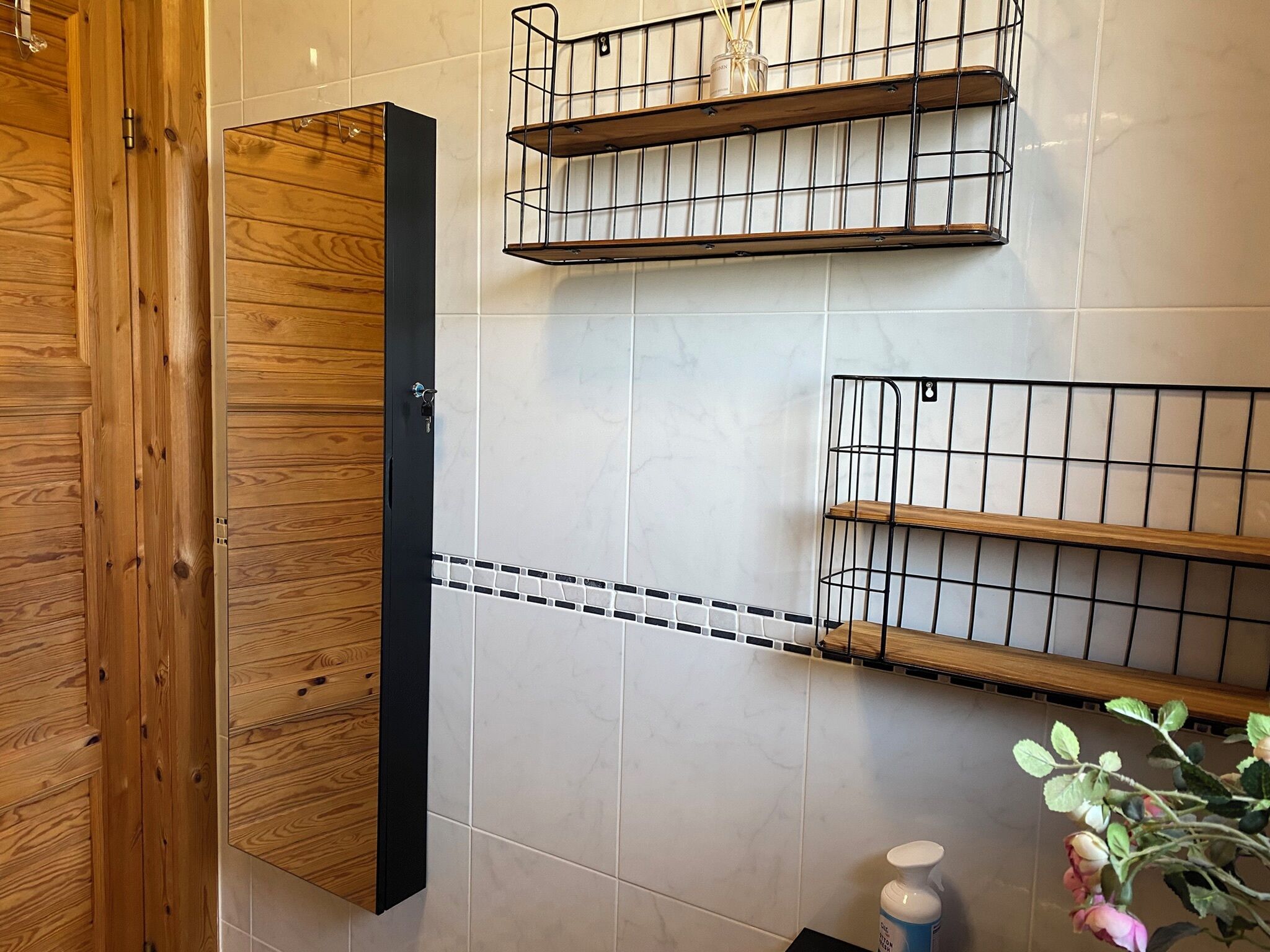 A bathroom with wooden cabinetry, tiled walls, and metal shelves.