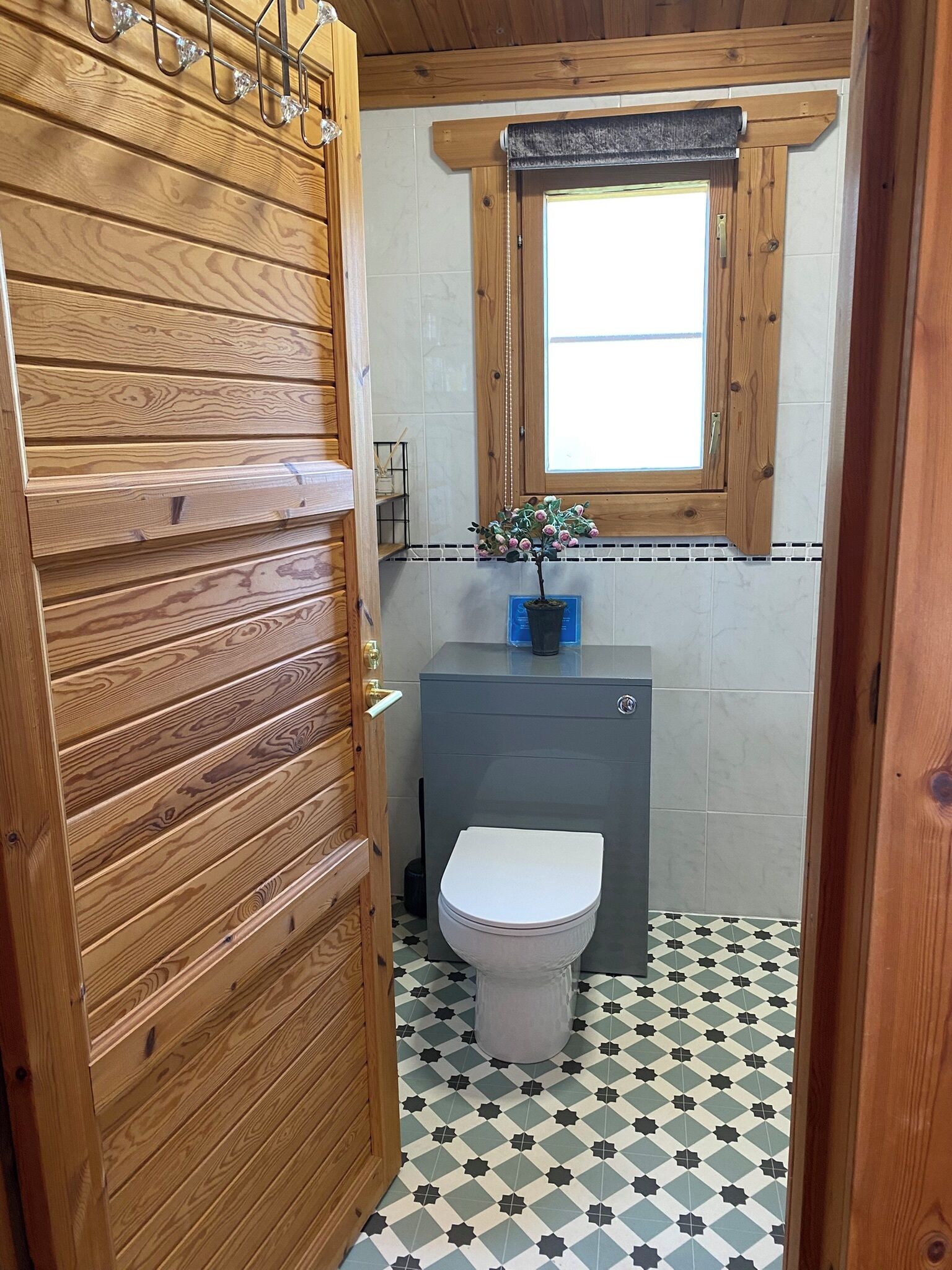 Een kleine badkamer met een houten deur, toilet, wastafel met een plant en een raam met houten kader.