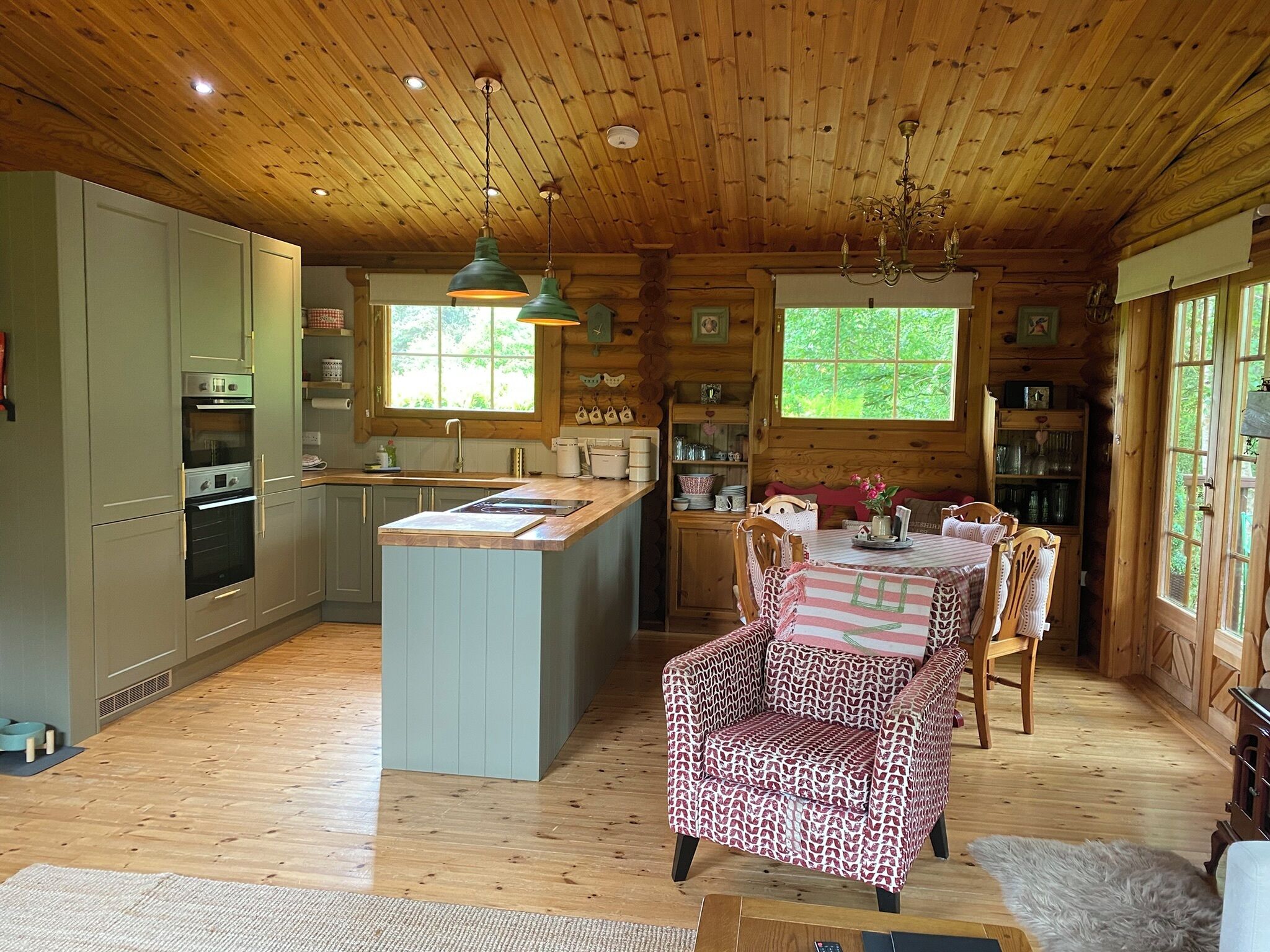 A wooden cabin interior with a kitchen, dining area, and a large window.