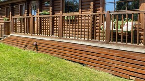 A log cabin with a wooden deck and a metal railing.