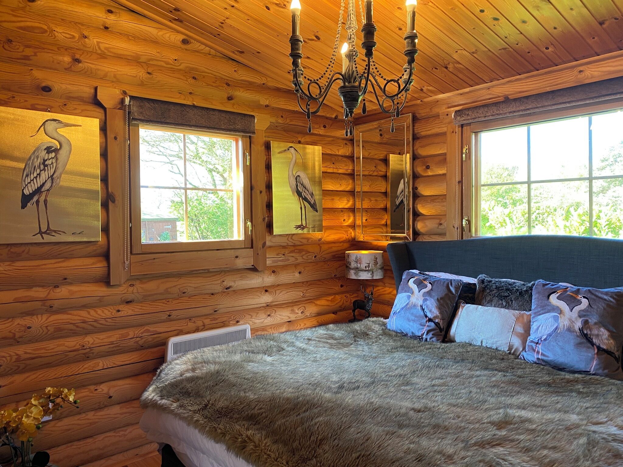 Une chambre située dans une cabane en rondins, avec un grand lit, des murs en bois et deux fenêtres.