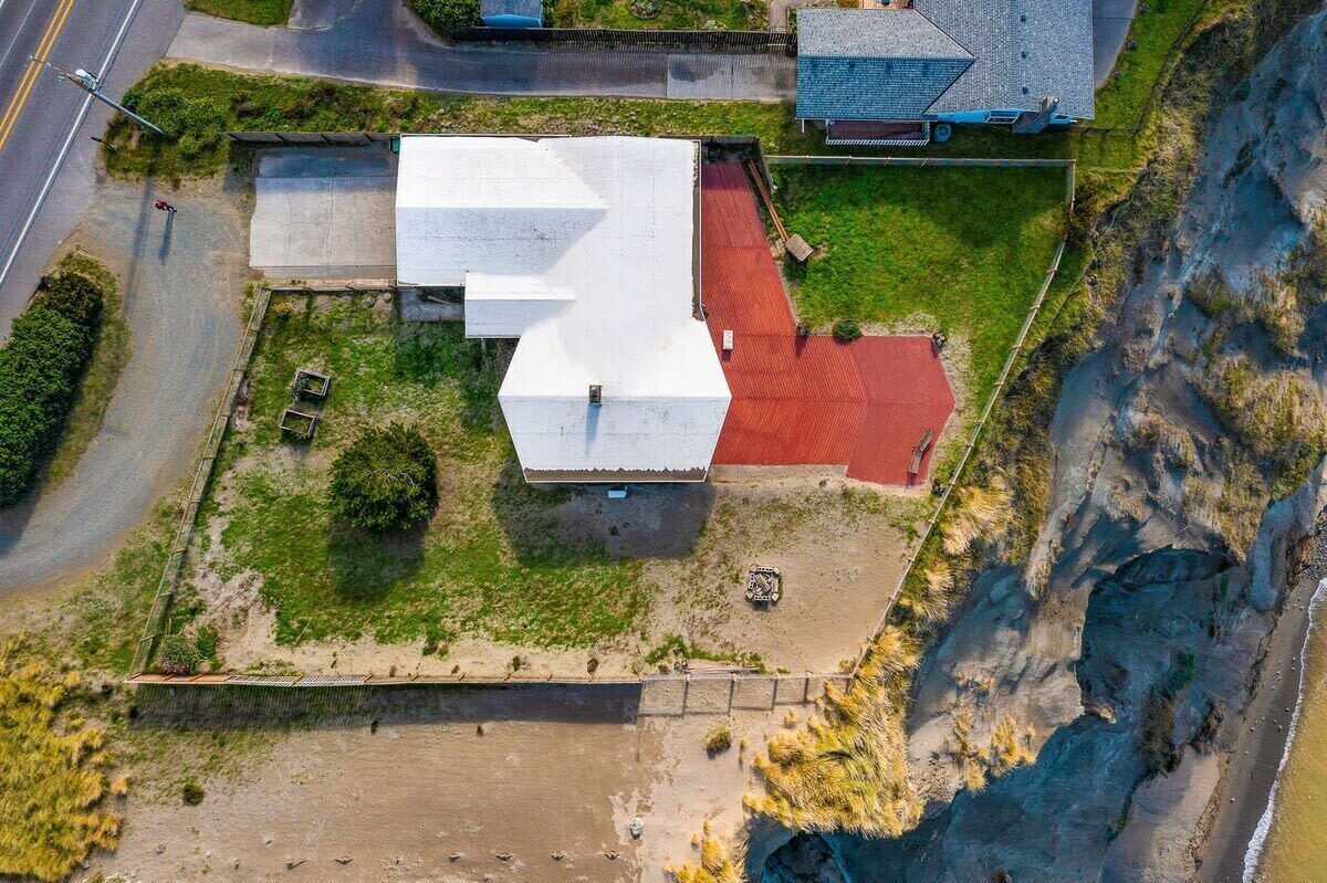 A building with a flat roof and a red roof section, surrounded by a grassy area and a cliff.