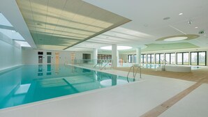 An indoor swimming pool with clear water, a tiled floor, and a ceiling with skylights.