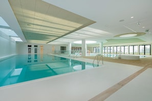 An indoor swimming pool with clear water, a tiled floor, and a ceiling with skylights.