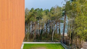 A view of a building with a wooden facade and a grassy area in the foreground.