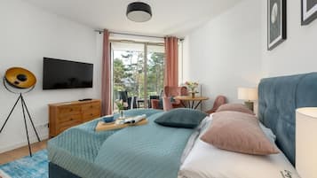 Ein modernes Schlafzimmer mit Bett, Fernseher, Schreibtisch und Fenster.