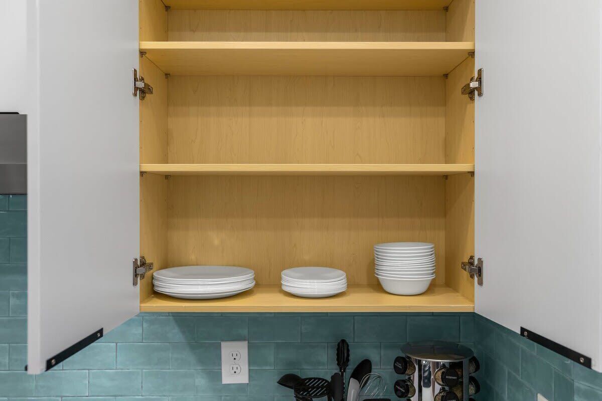 A kitchen with three wooden shelves, a countertop with a sink, and a backsplash.