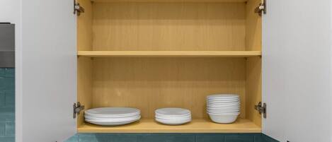 A kitchen with three wooden shelves, a countertop with a sink, and a backsplash.