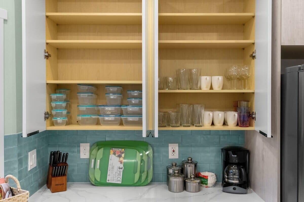 A kitchen with open cabinets, clear storage containers, and a coffee maker.