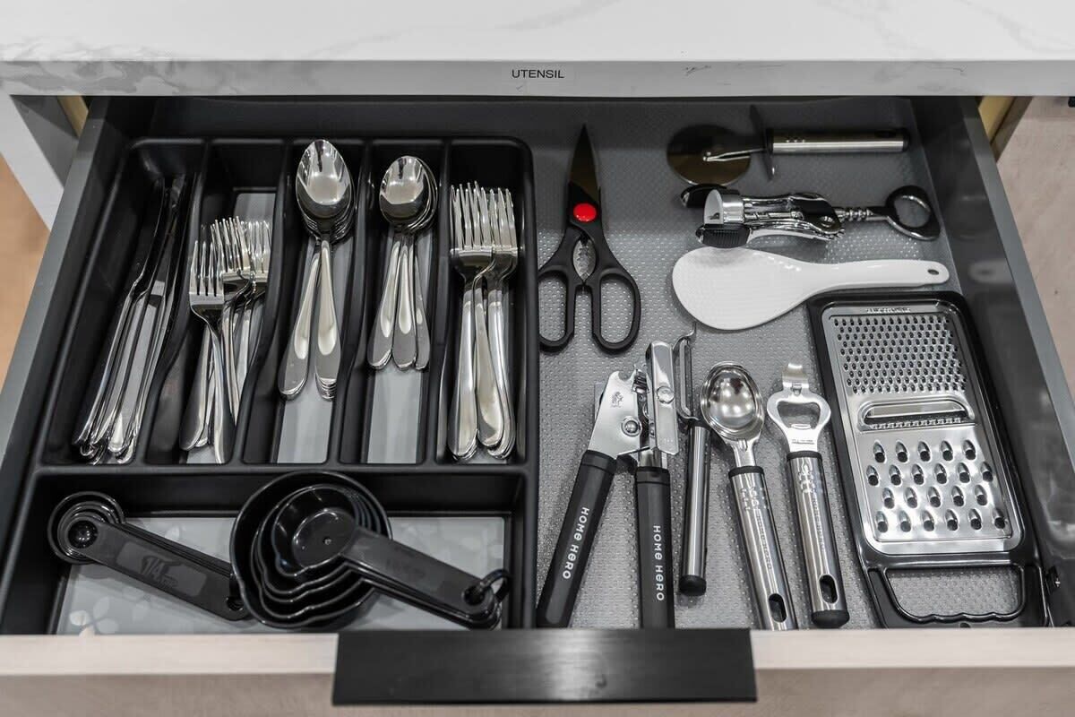 Un cassetto pieno di utensili da cucina, come forchette, cucchiai, coltelli, una grattugia e un macinapepe.