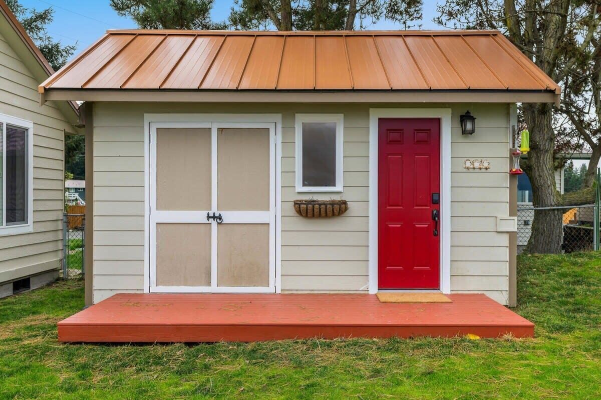 Un petit bâtiment d’un seul étage, avec une porte rouge, une fenêtre et un toit en métal.
