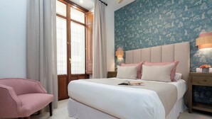 Ein Schlafzimmer mit einem großen Bett, einem rosa Sessel und einem Fenster mit Vorhängen.