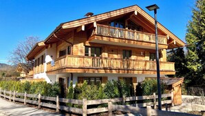 Eine mehrstöckige Holzhütte mit Balkonen, umgeben von einem Holzzaun und viel Grün.