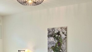 Ein Schlafzimmer mit einem hölzernen Bett, weißer Bettwäsche, einem an der Wand befestigten abstrakten Gemälde und zwei Nachttischlampen.