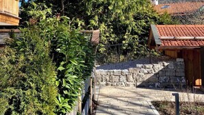 Ein Holzweg führt zu einem Gebäude mit einer Steinmauer und einer hohen Nadelbaum-Hecke.