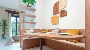 A modern dining area with a wooden table set for four, a built-in bench with cushions, and a wall-mounted shelf with decorative items. - Genteel Home San Vicente III (Seville)