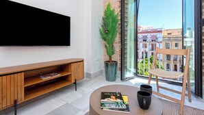 Un salon moderne avec un téléviseur à écran plat, un meuble de rangement en bois, une plante en pot, un fauteuil en osier et une table sur laquelle se trouvent un magazine et deux tasses.