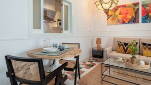 A dining area with a round table, chairs, and a chandelier. There is a sofa with cushions and a coffee table with a tray.