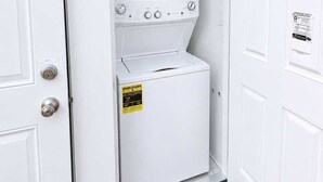 A laundry room with a washing machine and dryer, a door with a safety sign, and a brick floor. - @ Marbella Lane - Spacious 2BR Home Near Westgate  (San Jose)