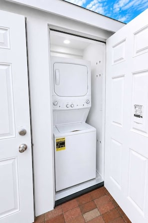 A laundry room with a washing machine and dryer, a door with a safety sign, and a brick floor. - @ Marbella Lane - Spacious 2BR Home Near Westgate  (San Jose)