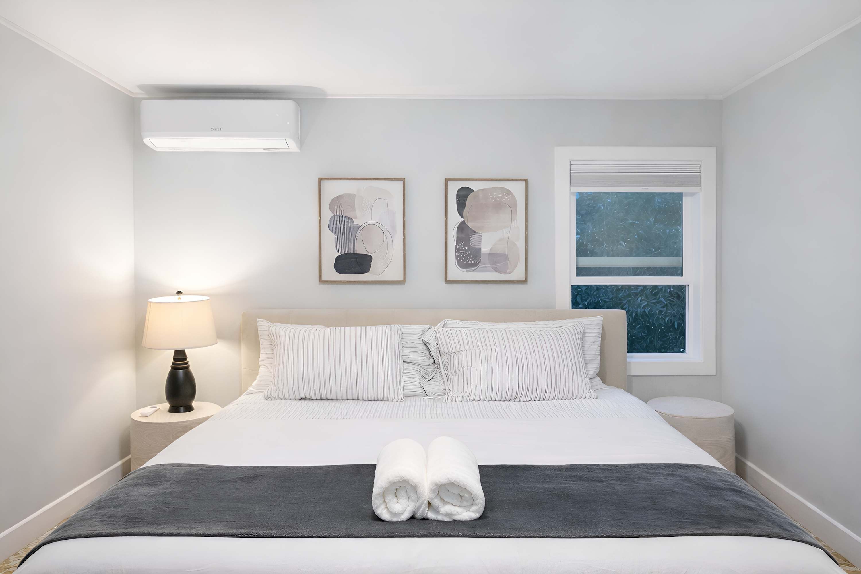 Hotelkamer met een bed, nachtkastje, lamp, twee ingelijste kunstwerken en een raam met uitzicht.