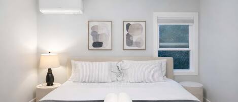 Hotelkamer met een bed, nachtkastje, lamp, twee ingelijste kunstwerken en een raam met uitzicht.