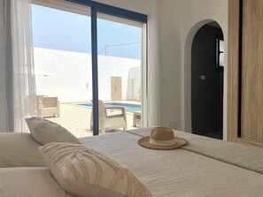 Une chambre dotée d’un grand lit, donnant sur une piscine, et dont la porte mène à une autre pièce.