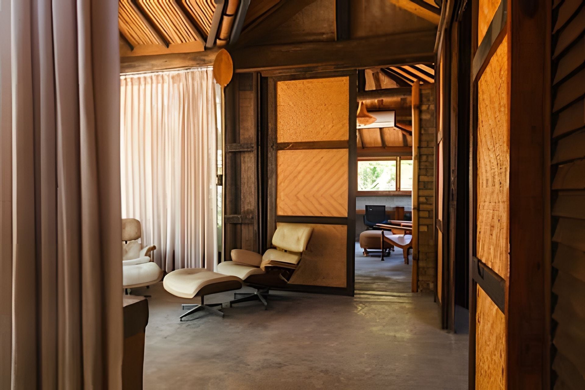 Um interior moderno com teto de madeira, uma janela grande e uma área de estar com duas cadeiras e uma mesa pequena.