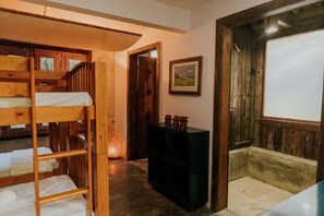 A room with bunk beds, a small black cabinet, a framed picture on the wall, and a wooden door leading to another room. - Ypê Greenhouse (Niteroi)