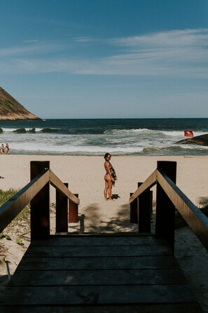 Una playa con escaleras de madera que bajan a la arena, una bandera de salvavidas y el océano al fondo.