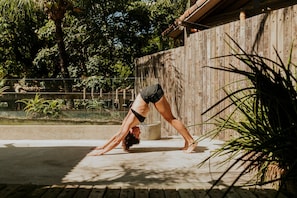 Iemand doet een yoga-houding in de open lucht, met een houten hek en begroeiing op de achtergrond.