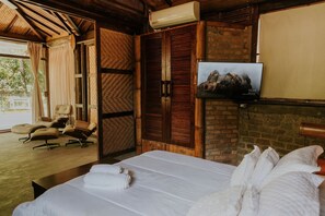A hotel room with a bed, a TV, a wooden wardrobe, and a seating area with chairs. - Ypê Greenhouse (Niteroi)