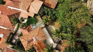An aerial view of a residential area with terracotta-roofed houses, lush greenery, and a central paved area. - Ypê Greenhouse (Niteroi)